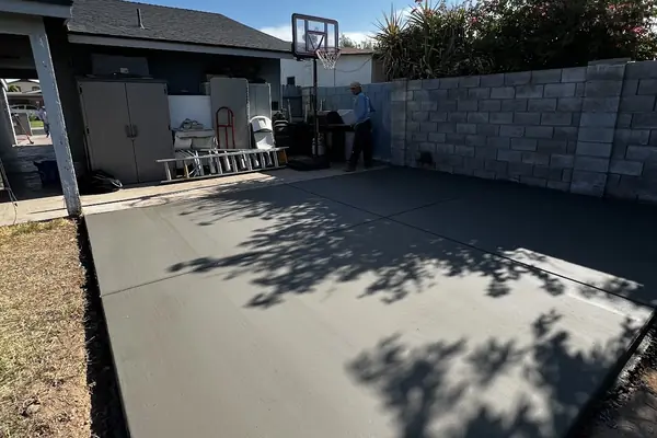A broom-finished backyard pad beside a block wall, poured by our featured contractor